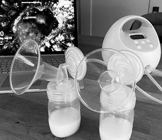 A breast pump machine sits on a desk in front of a laptop.