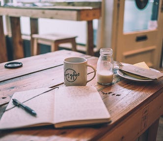 Wooden table featuring an open notebook, a mug and a bottle of milk.