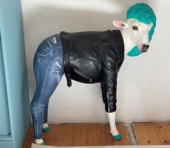 A goat, or maybe sheep, with green hair waiting jeans and a black leather jacket.