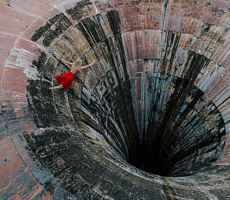 An aerial view of a colourful sinkhole and a blonde woman wearing a red dress about to fall into the hole.
