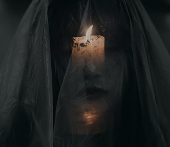 A lit candle shines through a woman’s sheer veil, casting light on her face.