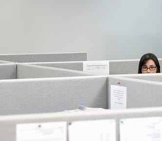 A woman peeks over a cubicle wall.