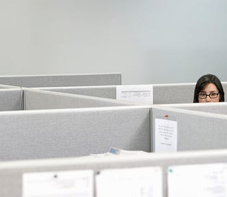 A woman peeks over a cubicle wall.