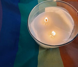 A white candle on a rainbow flag.