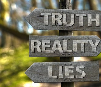 Image shows a wooden road sign with three words — truth, reality and lies. Truth and lies point to the left, reality to the right.