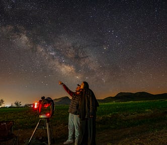 two people looking at a starry night sky with a telescope (searched engines)