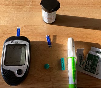 Picture of home diabetes testing equipment, including a monitor, alcohol swabs, test strips and a used lancet.