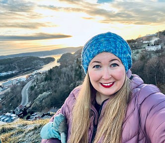 selfie of author in Halden, Norway with a scenic sunset background on a mountain with water below