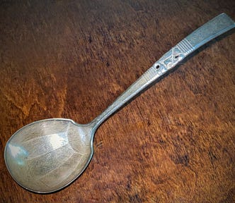 Large tarnished and scratched silver gravy ladle against a wood background.