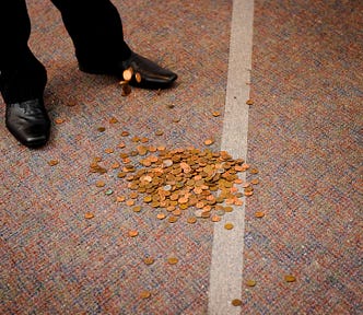 Pile of coins on the ground next to a man’s feet in dress shoes