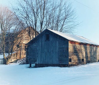 A brown wooden house near bare trees and in the snow during the daytime