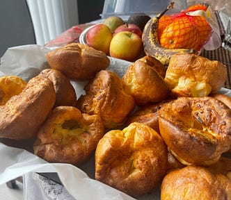 A basket full of rosemary popovers. In the background, there are apples and oranges.