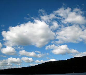 A blue sky with fluffy white clouds over a darkened shadow of a hill