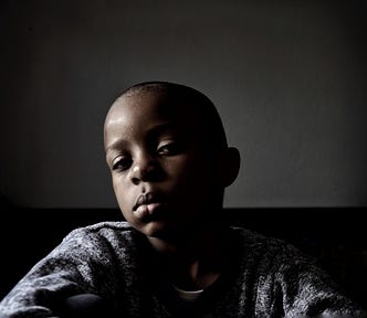 Shadowy portrait of a Black child with shaved hair.