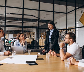 A group of young coworkers gathered around a table in a meeting room with glass windows.