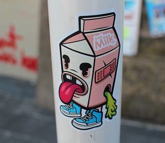 A sticker with a cartoon of a carton of milk with a face sticking its tongue out.