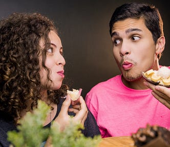 Young couple snacking on something and looking wide eyed at each other.