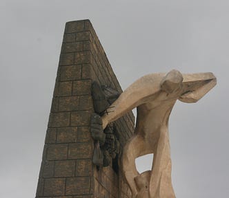 Color photo of a statue of a man in active life struggle on the side of a wall.