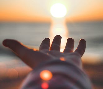 Outstretched hand at the beach at sunset, reaching toward the setting sun.