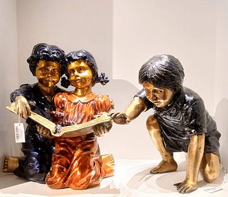 A sculpture of three kids, two reading a book and the third reaching out to them