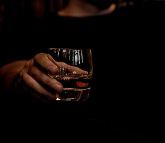 Dark picture with a hand holding a glass with whiskey in it.