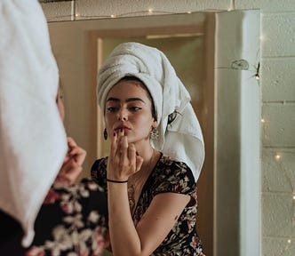 an image of a woman putting make-up in front of a mirror.