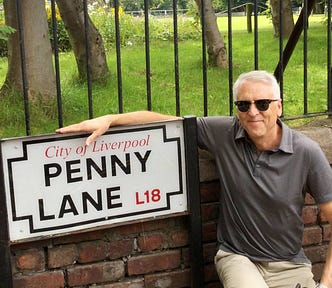 A man sitting next to the Penny Lane Road Sign