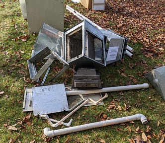 A photograph showing parts of an old HVAC system spread out on a lawn. There are fallen brown leaves on the grass, especially at the top right of the photo.
