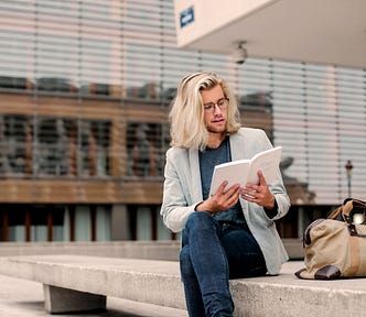 Long white haired formally dressed man reading a book outdoors