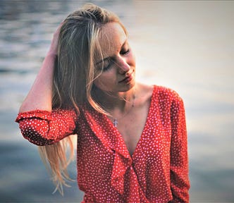 pensive girl with long blonde hair wearing red and white polka dot top with watery background