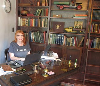 Woman at desk in office library with bookshelves and rolling ladder.