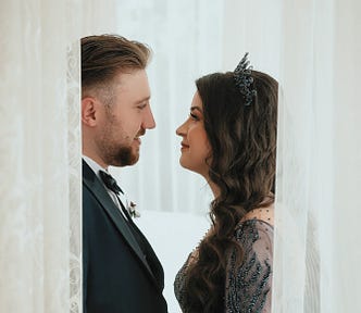 A man and a woman facing each other behind a sheer curtain. the curtain has an opening so they can see each other.