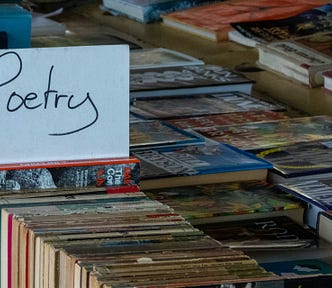 A tabe of used books. A handwritten sign in one stack reads “Poetry.”