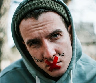 A hooded boy with his mouth taped shut with red duct tape in the shape of an X. And on his face is written: “Don’t lie”.
