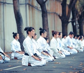 A row of people in karate uniforms sitting in meditation position