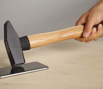 A photo of a man hitting a smartphone with a hammer.