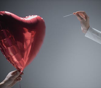 Heart balloon with a hand holding a needle ready to pop it.