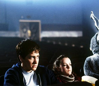 Donnie Darko, Gretchen, and Frank sit in an empty movie theater watching a film.