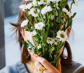 A woman holds up a bouquet of daisies in front of her face.