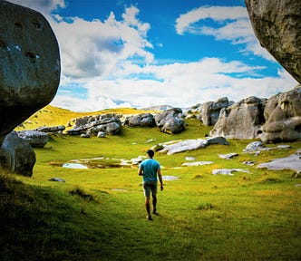 rear view of man walking through opening in huge boulders into grassy valley