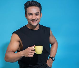 Smilingly douchey-looking person with hand on hip holding a yellow coffee mug