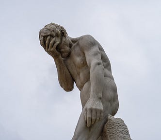 A statue of a male doing a face-palm against a cloudy-sky background