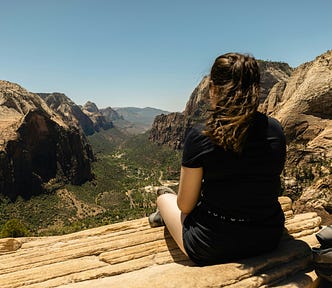A woman sitting on a rocky cliff ledge looking at at a valley below. Ridge of the world.