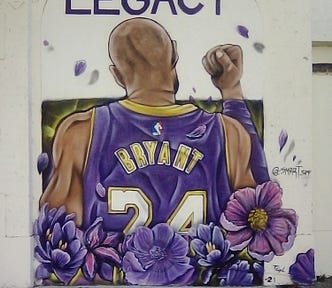 Street wall mural of Kobe Bryant (back of head) with purple flowers around.