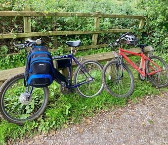 Two bikes leaning against a wooden fence in the countryside.