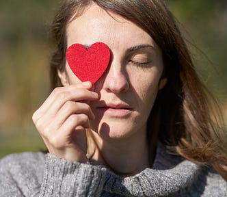 Woman holding a heart-shaped fabric over her right eye