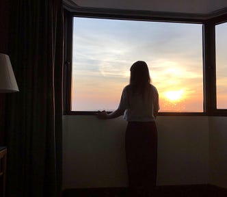A young woman looks out a window at sunset