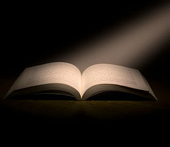 A shaft of light falls on the open pages of a book against a black background.