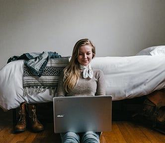 girl on laptop in front of bed