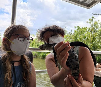 A ten-year-old boy with one of his moms. She is holding a baby alligator.